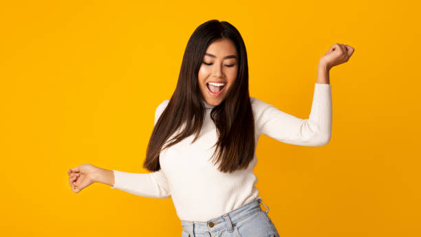 istock Happy asian woman dancing on yellow studio background 1189148215