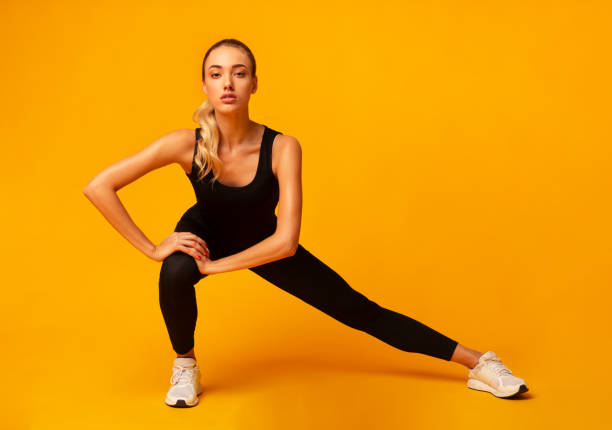 Fitness Woman Doing Side Lunge Stretch Working Out In Studio Determined Fitness Woman Doing Side Lunge Stretch Working Out In Studio Over Yellow Background. blonde female bodybuilders stock pictures, royalty-free photos & images