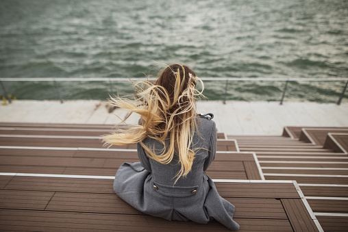 A rear view of a young blonde woman by the sea with wind moving her hair