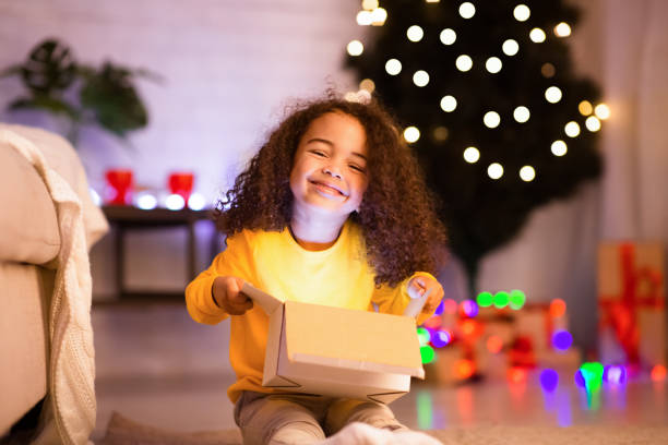 istock Cheerful afro child enjoying opening gift near Xmas tree 1189156738