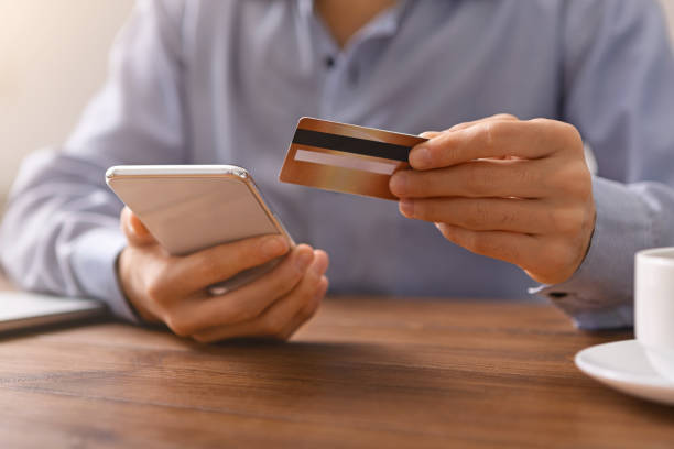 homme faisant des emplettes en ligne avec la carte de crédit et le smartphone au lieu de travail - beak buying currency exchanging photos et images de collection
