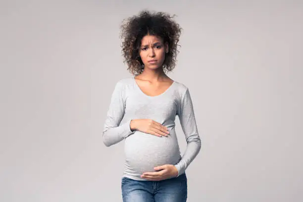 Photo of Tired pregnant woman embracing her belly, grey background