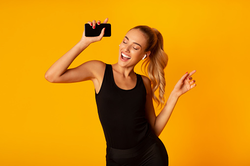 Mujer en auriculares inalámbricos sosteniendo Smartphone y bailando, tiro de estudio photo