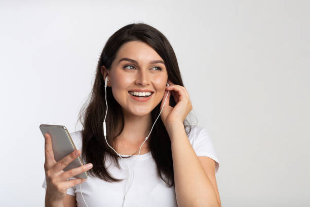 イヤホンの若い女性は、携帯電話で音楽を聴いて、白い背景 - young adult technology beautiful singing ストックフォトと画像