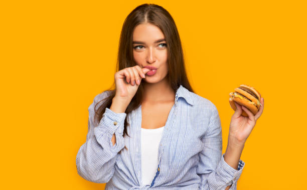 배고픈 소녀 들고 햄버거 위에 서 노란색 배경 - finger licking 뉴스 사진 이미지