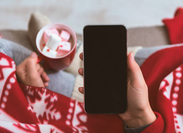 Woman with cellphone in hand drinking chocolate with marshmallow