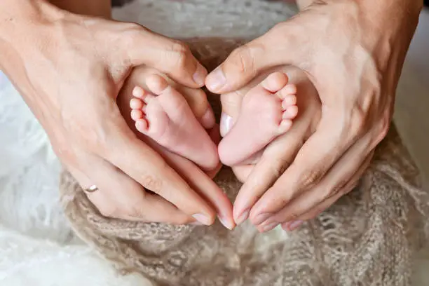Children's feet in hands of mother and father. Feet of the tiny Newborn Child on a close up of hands of a warm form. Mother, father and Child. Happy Family concept. Beautiful conceptual image of Motherhood