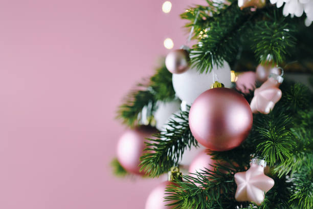 Close up of decorated Christmas tree with white seasonal and pink tree ornaments like baubles and stars on pink background with lights in background christmas tree pink christmas tree stock pictures, royalty-free photos & images