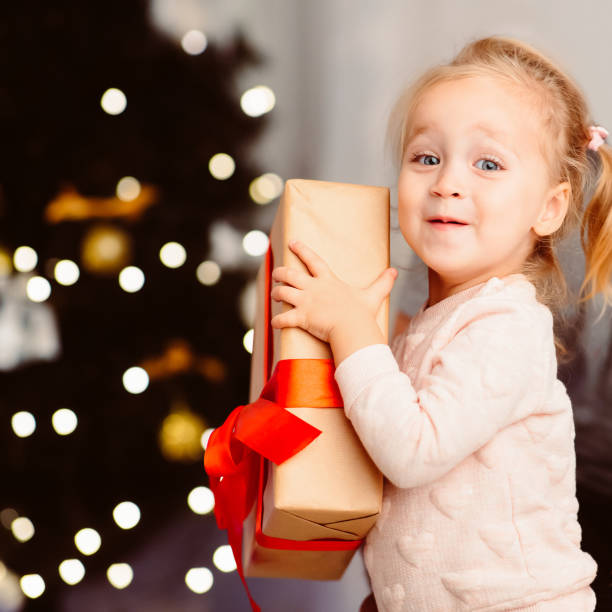 istock Adorable toddler holding present box near xmas tree 1189160575