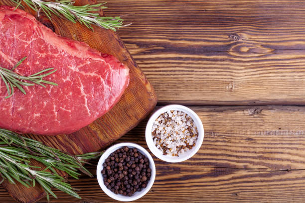 istock Raw Fresh Steak Served with Rosemary and Herbs on Rustic Wooden Board 1189162744