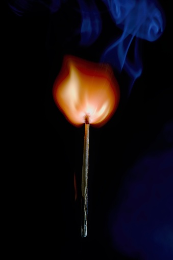 Vertical photo of match stick. The safety match has flaming hot head but the body is still fine. Nice curly smoke goes from head to the space. Background is black.