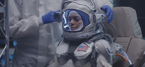 Medium close-up of a scientist helping a young female astronaut to get ready for a spaceflight