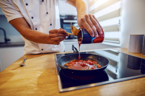 istock Close up of creative experienced caucasian chef in uniform adding peeled tomato. Domestic kitchen interior. 1189168418