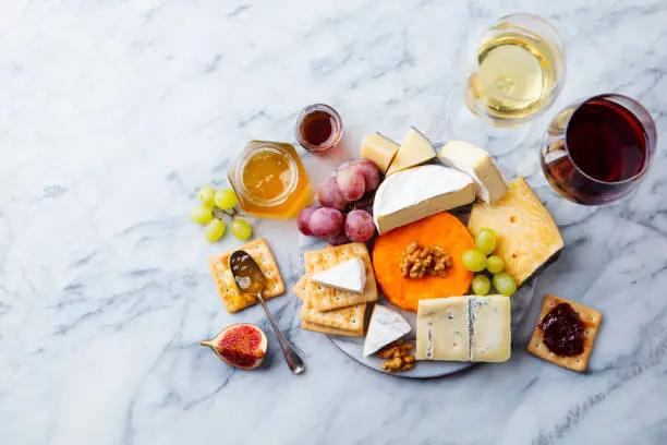 Photo of Assortment of cheese, grapes with red and white wine in glasses. Marble background. Top view. Copy space.