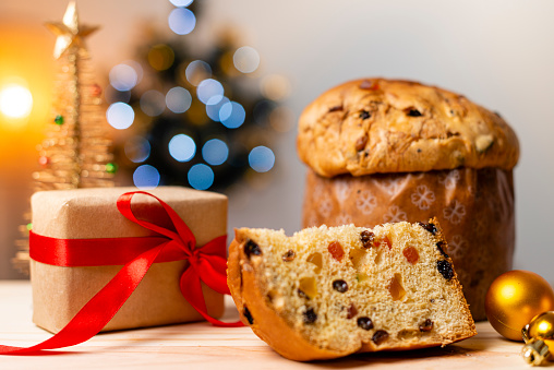 Delicious Panettone slice with candied fruits with blinking blurred christmas lights. Dry fruits. Gifts with Christmas ornaments.