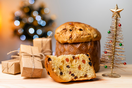 Delicious Panettone slice with candied fruits with blinking blurred christmas lights. Dry fruits. Gifts scattered on the table.