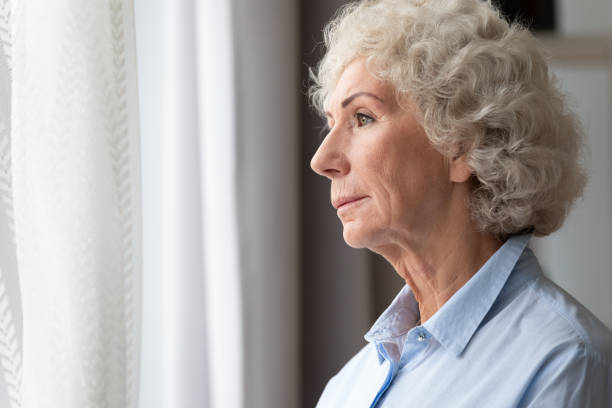 Pensive thoughtful lonely senior grandma looking through window