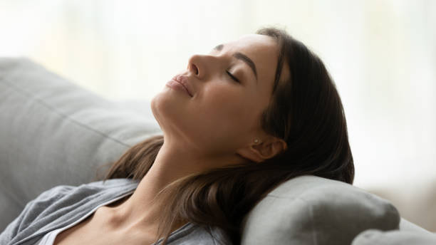 Beautiful healthy young woman taking deep breath of fresh air Beautiful healthy young woman taking deep breath of fresh air relaxing napping on comfortable couch, attractive calm lady meditating enjoying resting on sofa feel peace of mind at home, close up view eye reflection stock pictures, royalty-free photos & images