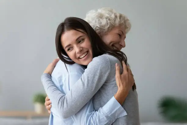 Happy young lady adult daughter granddaughter visiting embracing hugging old senior retired grandmother cuddling bonding, two age generations women expressing love and care at reunion meeting at home