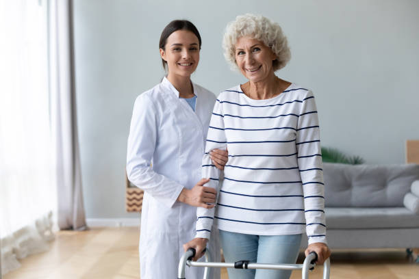 istock Female physiotherapist help old woman using walker look at camera 1189188579