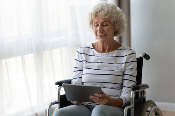 istock Happy disabled senior woman sit on wheelchair using digital tablet 1189188600