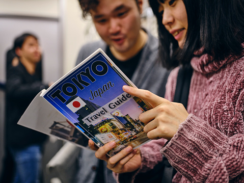 Young People Reading a Guidebook amongst a crowd of people on a Japanese subway train. Fully property released location.