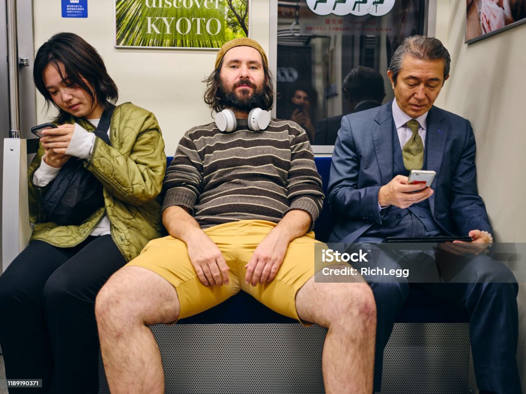A Man Taking Up Space on a Crowded Japanese Subway Train A man spreading out and taking up too much space amongst a crowd of people on a Japanese subway train. Fully property released location. Manspread Stock Photo