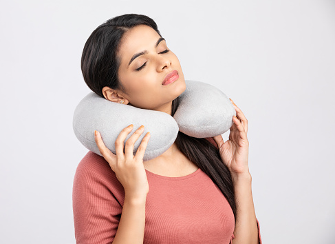 Young woman with a neck pillow on white.