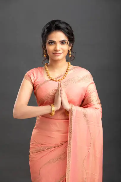 Pretty Indian young woman greeting in traditional saree on white.