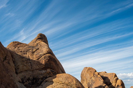 Sierra Nevada California desert rock formations of the Alabama Hills of the town of Lone Pine with white stripes of clouds in blue sky