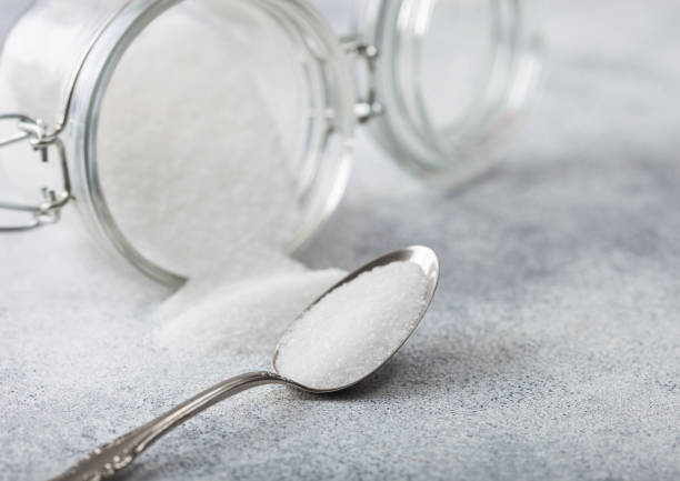 istock Glass jar of natural white refined sugar with silver spoon on light table background. 1189219156