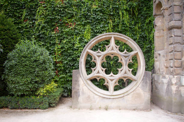 Architectural element of medieval cathedrals is a round granite window with a Gothic rose in the background of a green park.