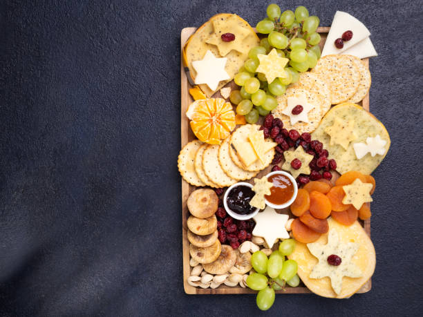 istock Cheese board appetizers platter with various types of cheese plate, grapes, dried figs, cranberries, pistachios and jams on dark background. Overhead view, free space. 1189222801