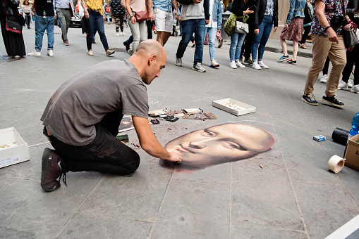 Street painter drawing a Mona Lisa while people are passing by on a street of Florence, Italy. Horizontal outdoors full length shot.