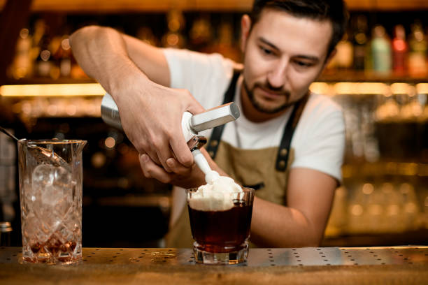 bartender adds whipped cream to alcohol cocktail - drink close up dairy product flowing imagens e fotografias de stock