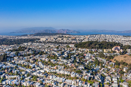 An aerial view over the city of San Francisco on a sunny day. Majestic view as we look over the city with parks, row houses , iconic buildings and the Golden Gate Bridge in the distance. The entire city is in view.