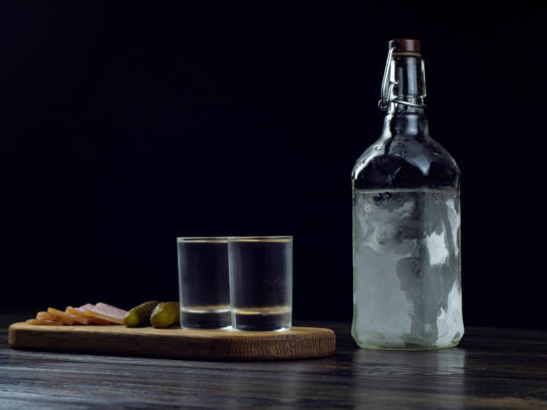 bottiglia di vodka, due bicchieri nebbiati con vodka fredda su una tavola di legno con pancetta e cetrioli sottaceto. tradizionale spuntino russo - russian shot foto e immagini stock