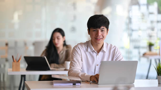 istock Asian man sitting on office workplace with laptop computer and looking at camera. 1189265443