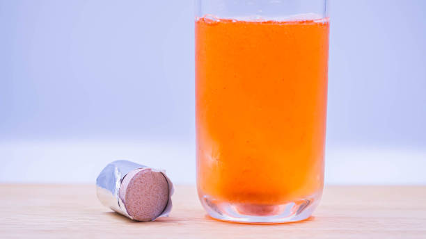 Closeup of multivitamin effervescent tablet pills and a glass of cold water with sparkling fizzy bubbles on wooden table and gray blurry bedroom background. stock photo