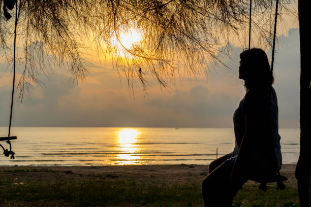 istock A woman sits on swing, looking at sunrise on beachfront 1189292690