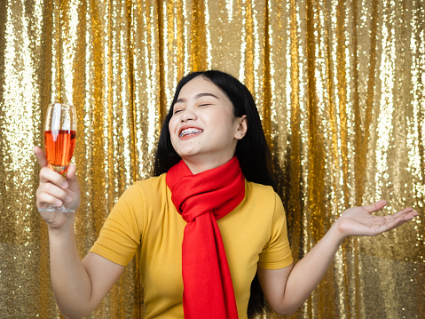 Happy Asian woman with red scarf and drinking red wine on gold glitter background.
