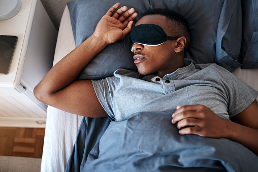 Cropped shot of a handsome young man wearing a night mask and sleeping in his bed at home