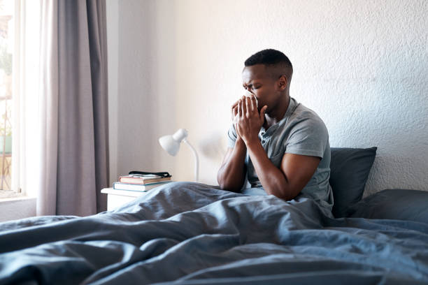 I'm sick again! Cropped shot of a handsome young man sitting in his bed and blowing his nose while suffering from a cold blowing nose photos stock pictures, royalty-free photos & images