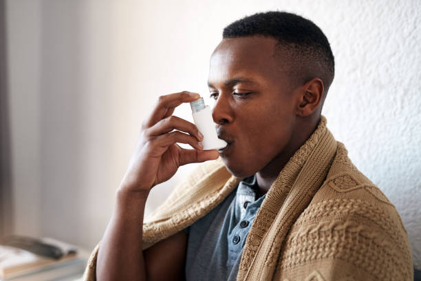 I really need my asthma pump Cropped shot of a handsome young man sitting alone in his bedroom and using an asthma pump asthma inhaler stock pictures, royalty-free photos & images