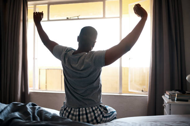 Let's get this day started Cropped shot of an unrecognizable man sitting on his bed alone and stretching during a day off at home wake water stock pictures, royalty-free photos & images
