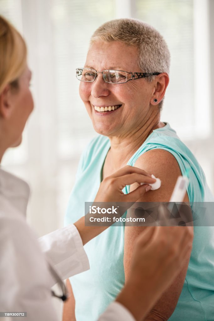 Doctor disinfecting patient's arm before vaccination Senior woman receiving vaccine at the doctor's office. Flu Vaccine Stock Photo