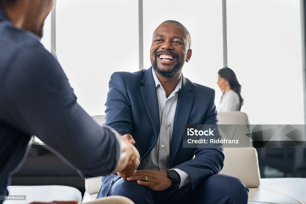 Business people shaking hands Two happy mature business men shaking hands in modern office. Successful african american businessman in formal clothing closing deal with handshake. Multiethnic businessmen shaking hands during a meeting. Handshake Stock Photo