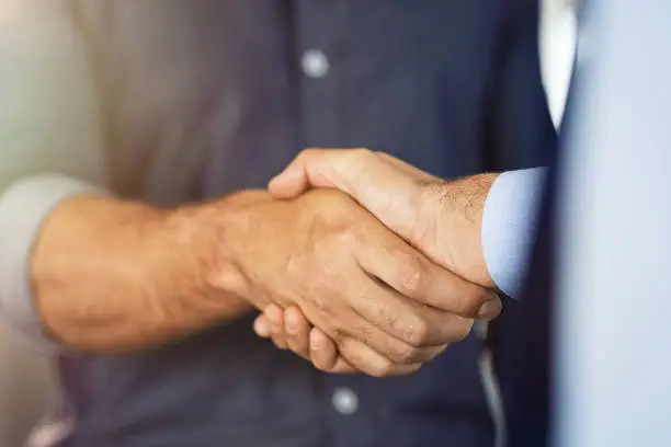 Close up of friendly handshake of business people. Business partners signing deal with handshake at office. Negotiation meeting for a successful merger, business agreeement.