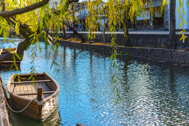 Traditional wooden boat docked on the river bank with willow trees. Kurashiki River, Okayama, Japan