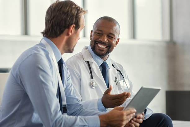 Multiethnic specialist doctors discussing case Two mature smiling doctors having discussion about patient diagnosis, holding digital tablet. Successful african surgeon discussing case after positive result. Representative pharmaceutical discussing with african happy doctor about new medicine. doctors office stock pictures, royalty-free photos & images